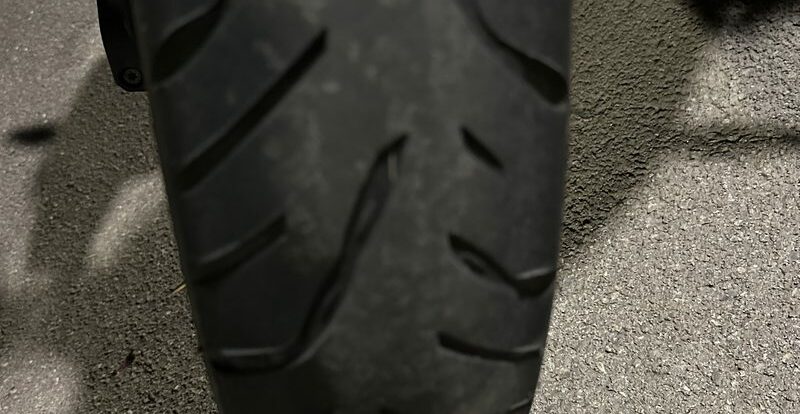 Pneu avant de moto à la gomme usée photographié de face sur le bitume