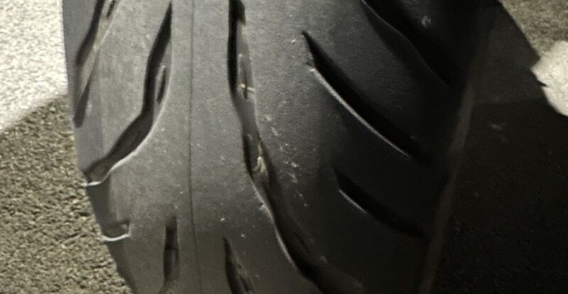 Gros plan d'un pneu moto très usé montrant des sculptures presque effacées