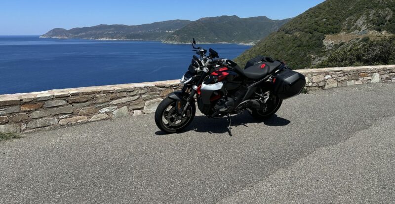 Roadster équipé de valises sur une route côtière surplombant la mer corse