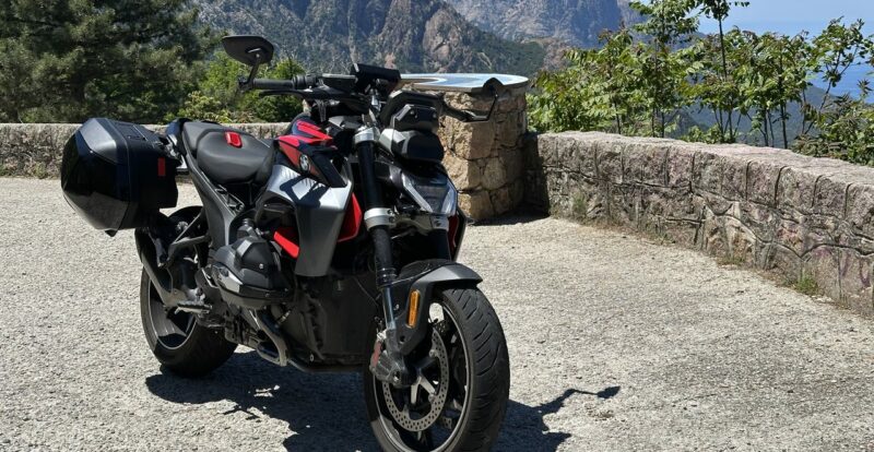 Moto roadster de profil à un belvédère devant les sommets escarpés des calanques corses