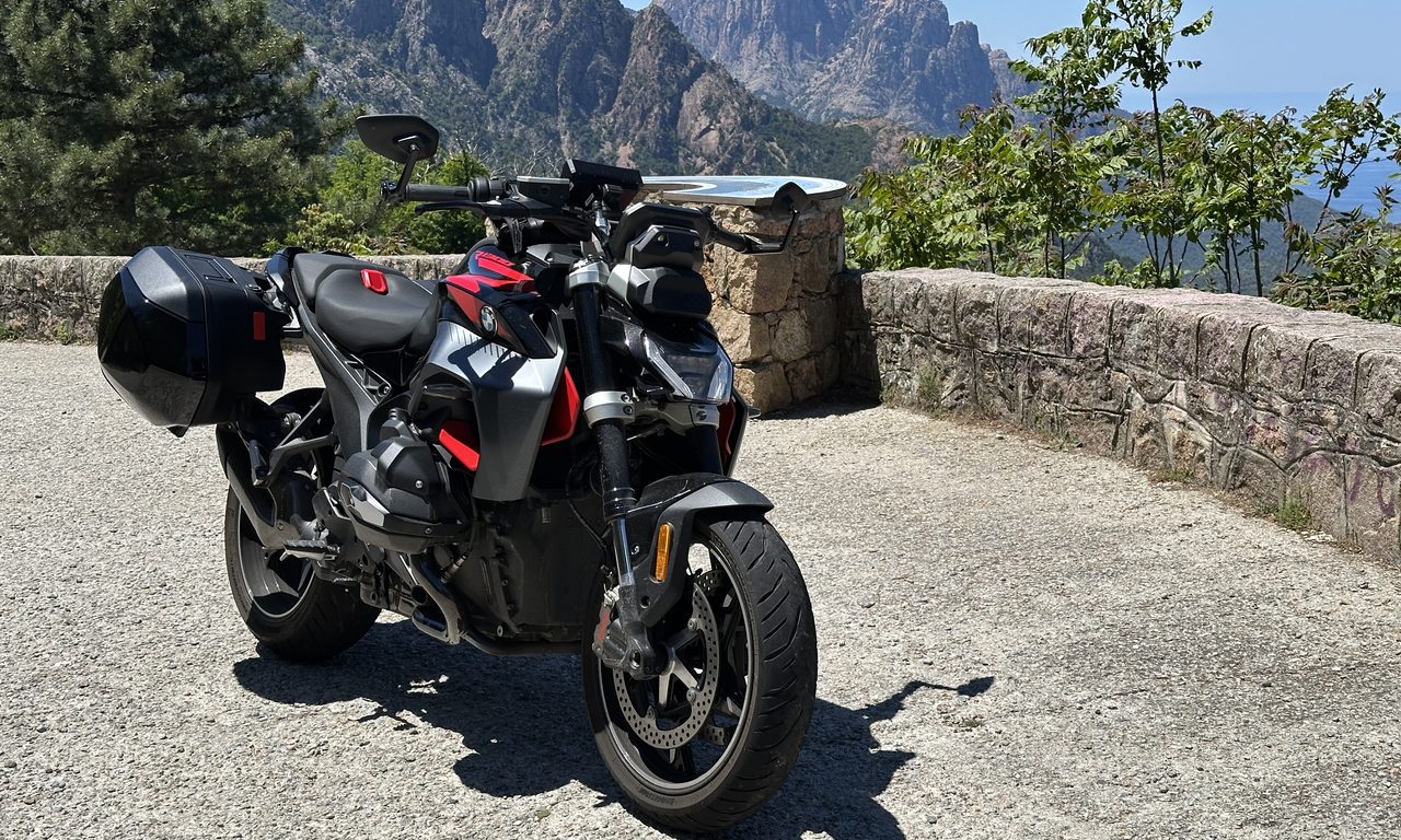 Moto roadster de profil à un belvédère devant les sommets escarpés des calanques corses