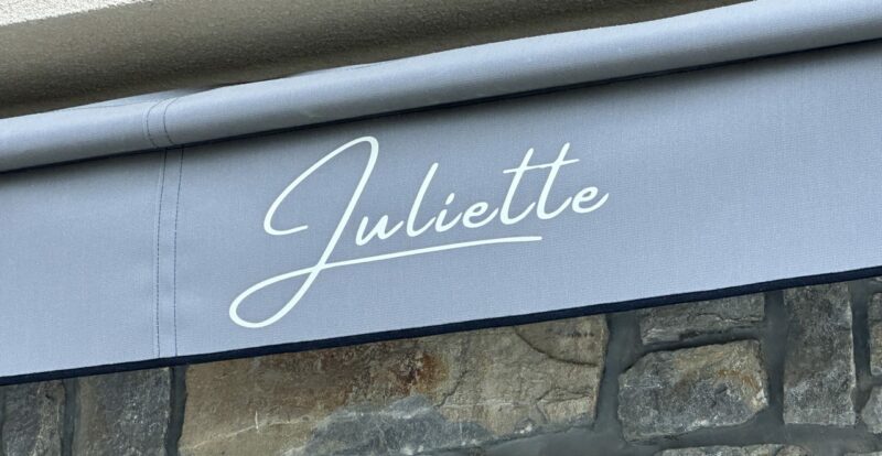 Store banne gris floqué Juliette au-dessus d'un mur en pierre
