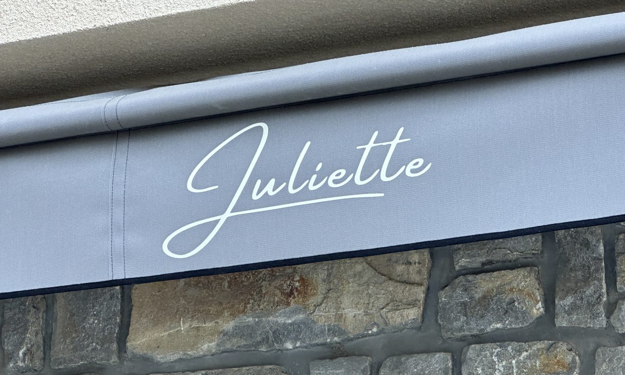 Store banne gris floqué Juliette au-dessus d'un mur en pierre