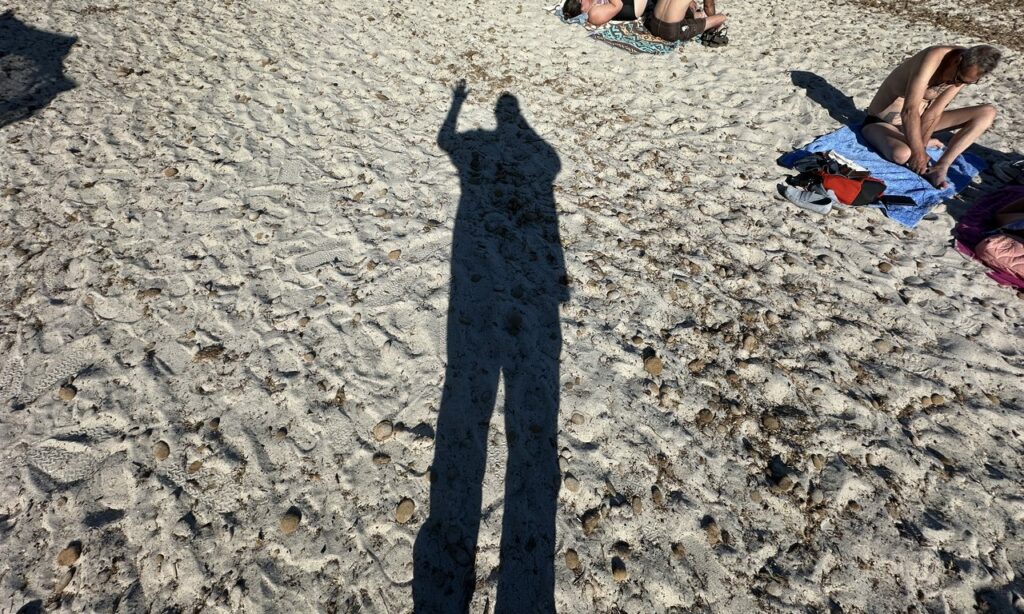 Ombre du motard saluant sur le sable blanc d'une plage corse ensoleillée