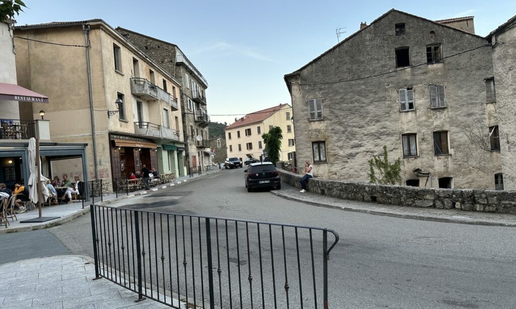 Place de village corse avec restaurant en terrasse et maisons anciennes