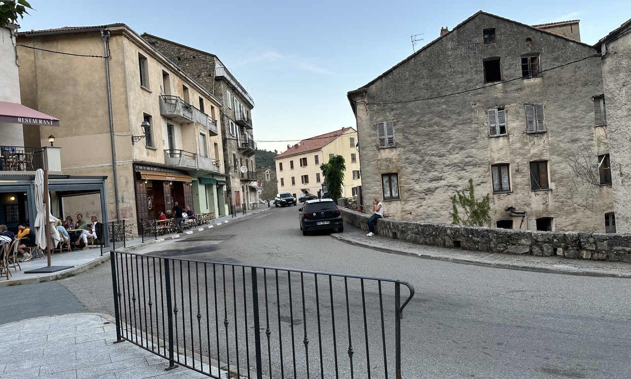 Place de village corse avec restaurant en terrasse et maisons anciennes