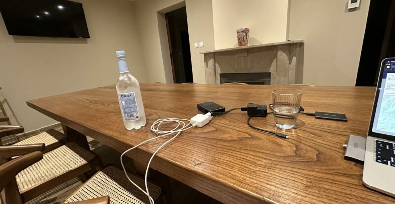 Grande table en bois avec bouteille d'eau Orezza, chargeurs et caméra