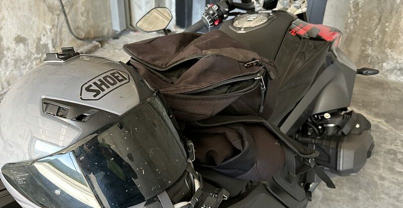 Casque Shoei et bagages posés sur la moto stationnée contre un mur de pierre