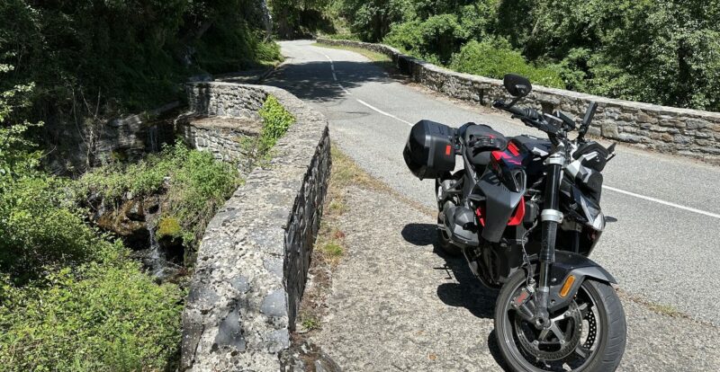 Roadster sur un pont de pierre, route sinueuse et ruisseau en contrebas