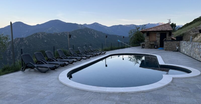 Piscine à débordement face aux montagnes corses au crépuscule avec transats