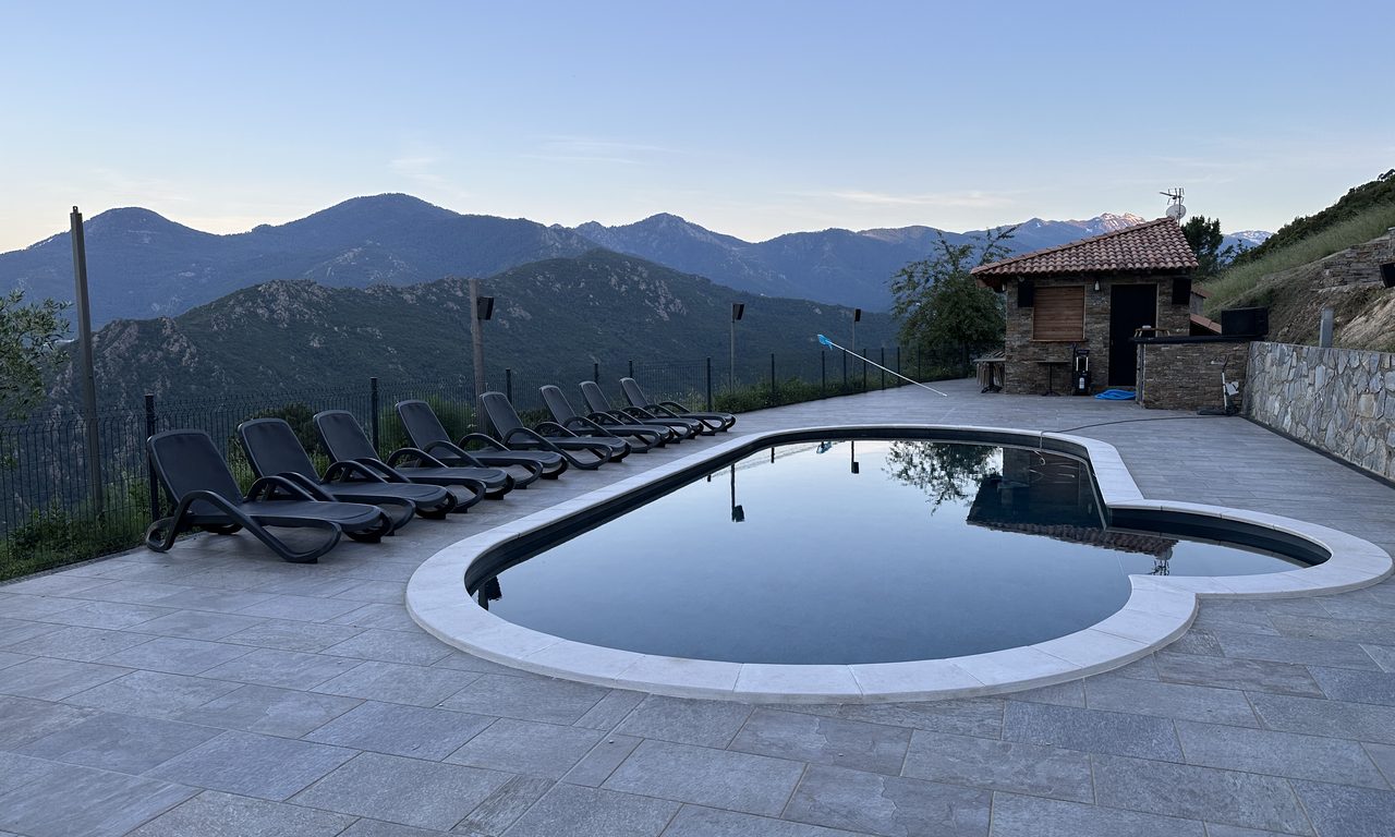 Piscine à débordement face aux montagnes corses au crépuscule avec transats