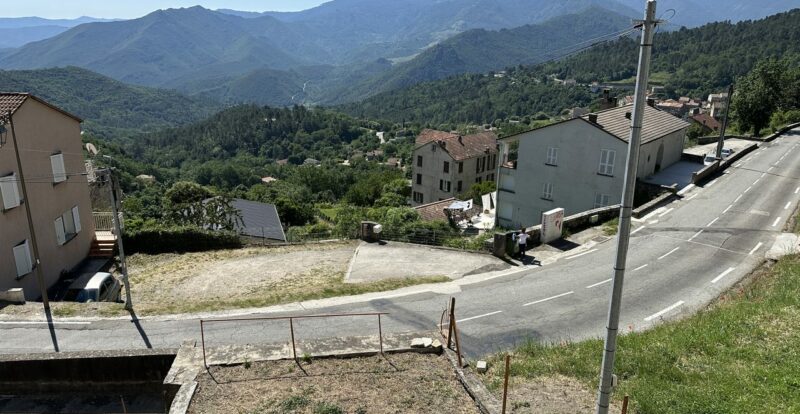 Village corse perché avec maisons et route sinueuse face aux montagnes boisées
