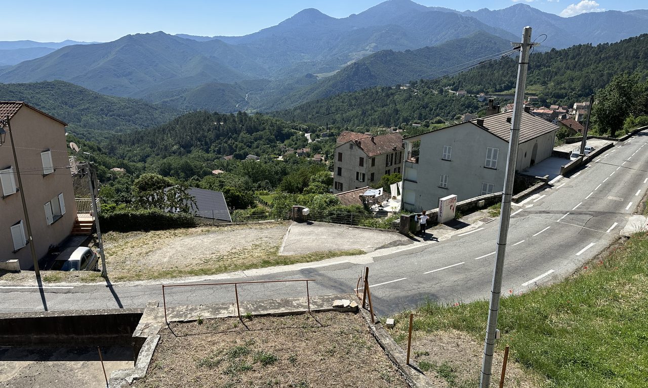 Village corse perché avec maisons et route sinueuse face aux montagnes boisées