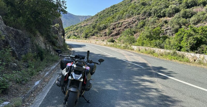 Moto à l'arrêt sur une route de montagne corse bordée de maquis et rochers
