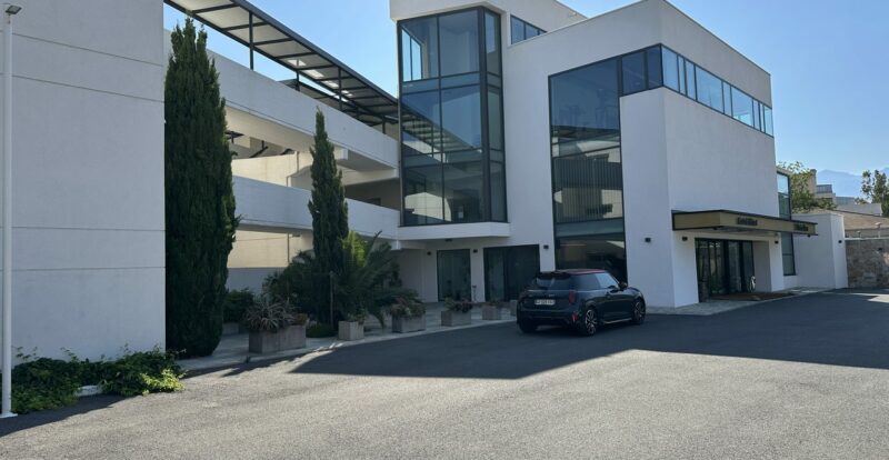 Hôtel moderne corse aux lignes blanches avec cyprès et Mini garée devant l'entrée