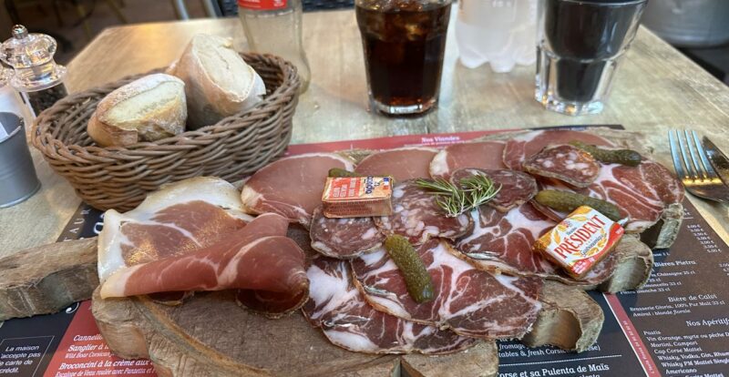 Planche de charcuterie corse avec coppa, lonzu, pain et cornichons sur table de restaurant
