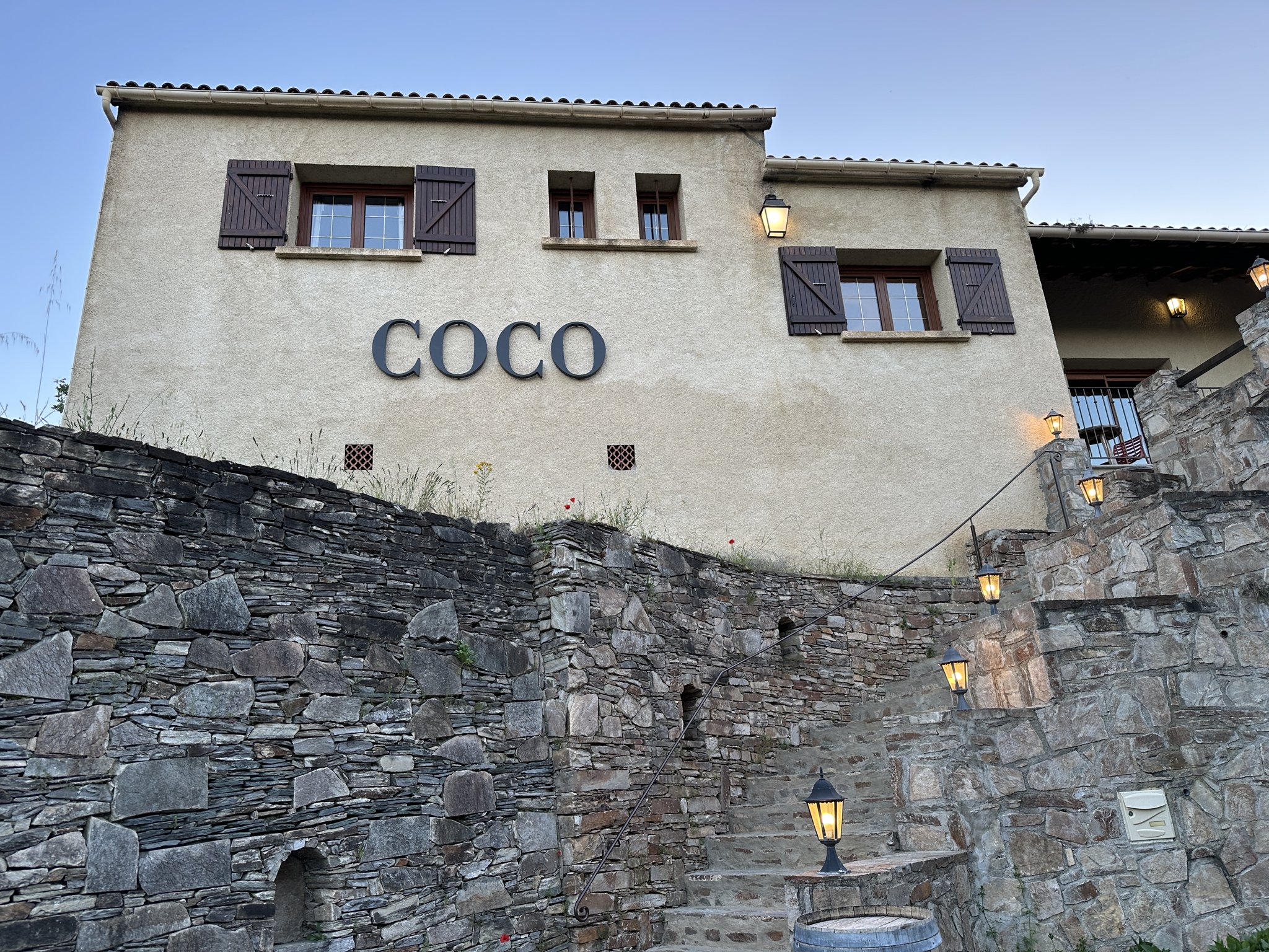 La façade de Chez Coco à Venaco, pierre et volets bruns à la tombée du jour.